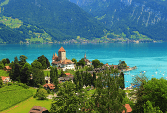 Scenic view of a serene lake surrounded by majestic mountains in Switzerland. Clear blue water reflects the surrounding landscape, creating a picturesque setting
